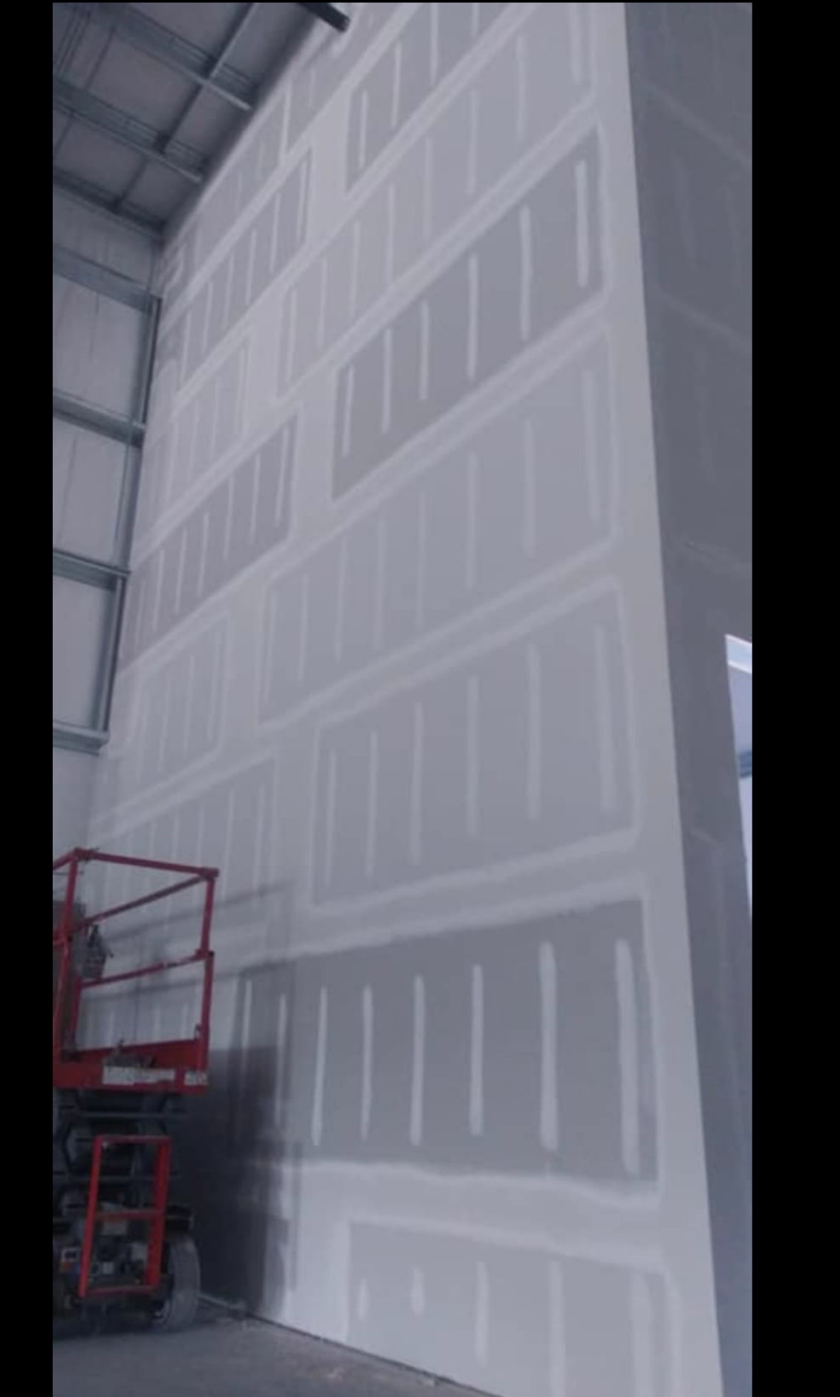 Two-story commercial warehouse wall taped and coated from a scissor lift, every seam and fastener uniformly floated