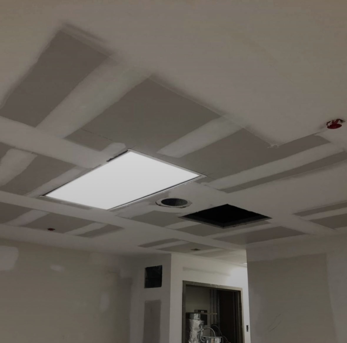Suspended ceiling grid area with drywall soffits taped around light panels, vents and sprinkler heads