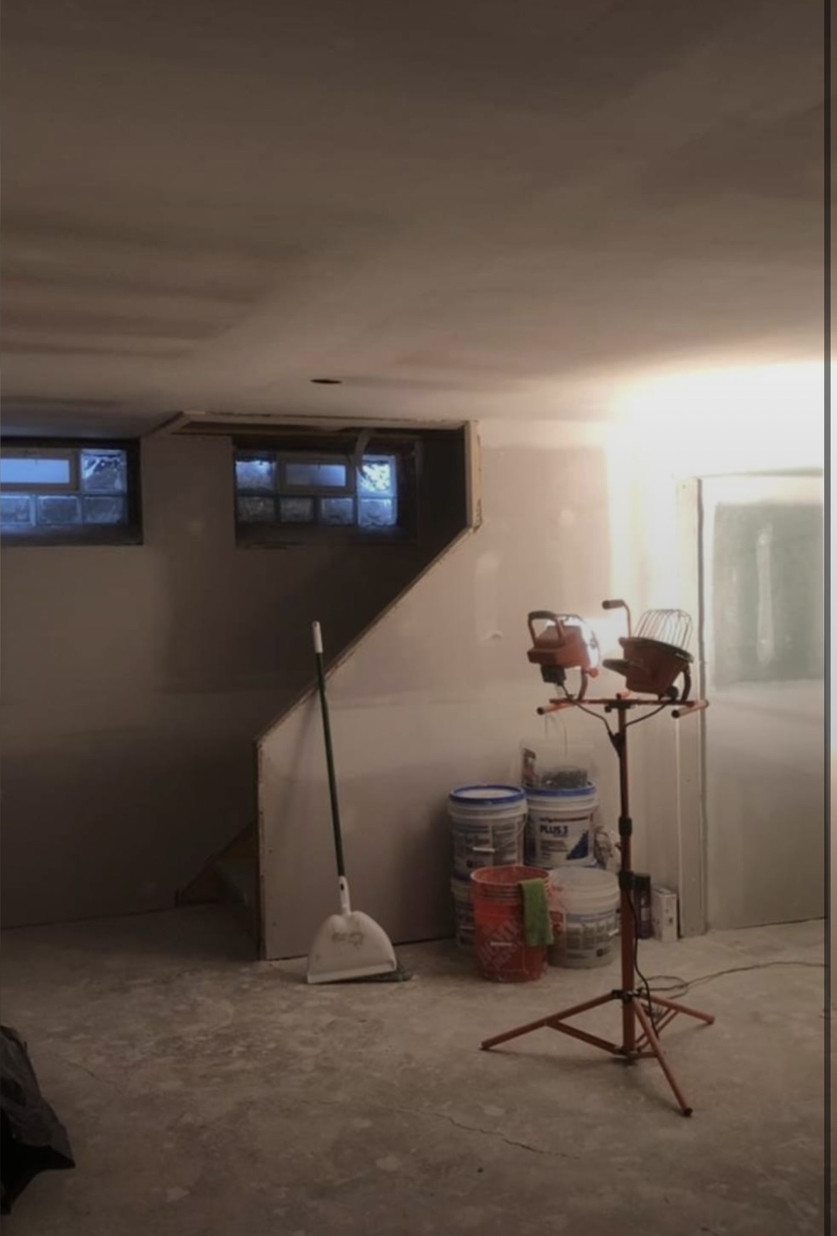 Basement stairwell and ceiling finished to a uniform level 4 surface with work light and mud buckets on site